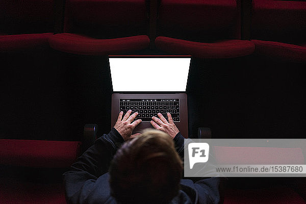 Regisseur sitzt im Theatersaal und arbeitet am Laptop  Draufsicht