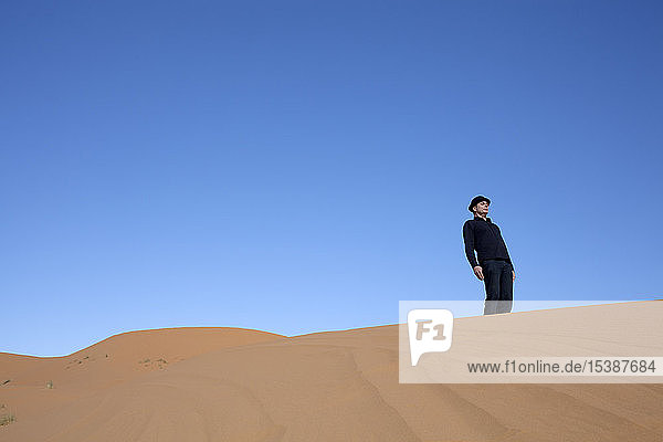 Morocco  Merzouga  Erg Chebbi  man wearing a bowler hat standing crooked on desert dune