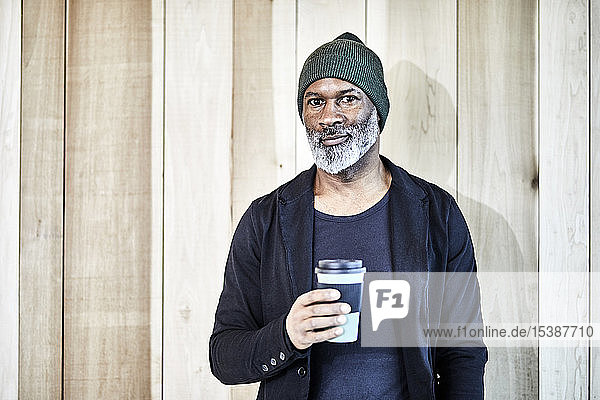 Porträt eines selbstbewussten reifen Geschäftsmannes mit Kaffee zum Mitnehmen an der Holzwand