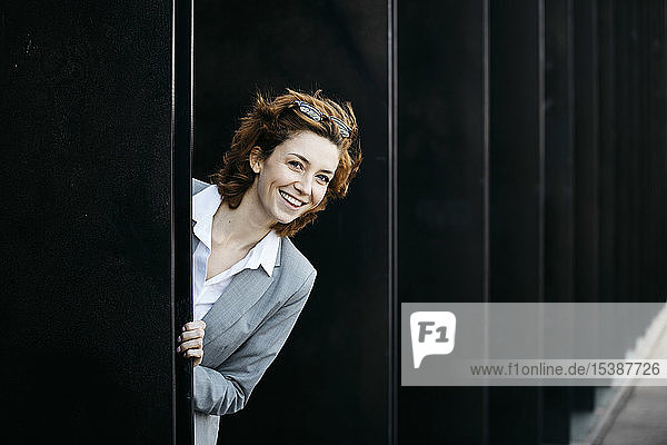 Glückliche junge Geschäftsfrau schaut aus der Fassade eines Bürogebäudes