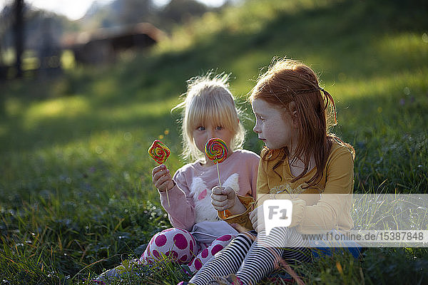 Zwei Schwestern sitzen auf einem Feld und halten Lollipops