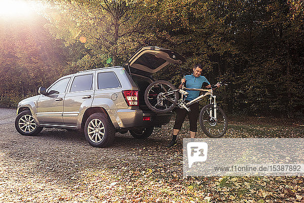 Man on foreat car park unloading mountainbike from car