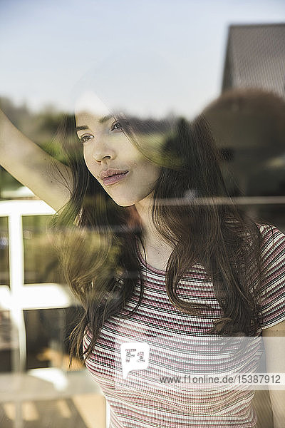 Porträt einer nachdenklichen jungen Frau hinter einer Fensterscheibe