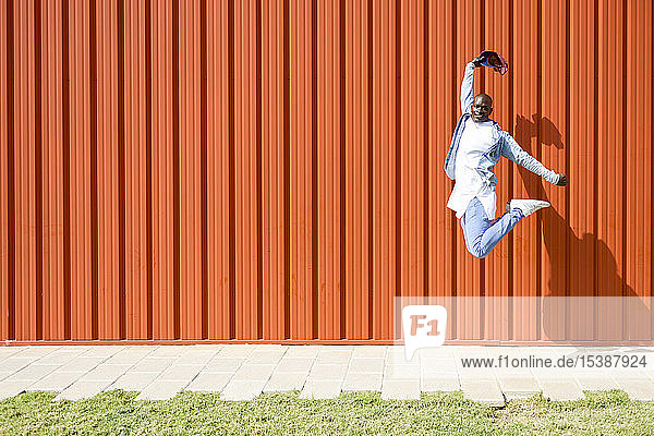 Mann in lässiger Jeansbekleidung springt vor orangener Wand in die Luft