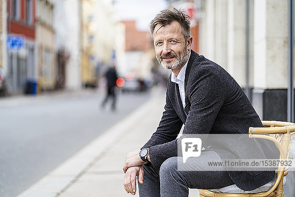 Portrait of smiling mature businessman sitting on a chair in the city