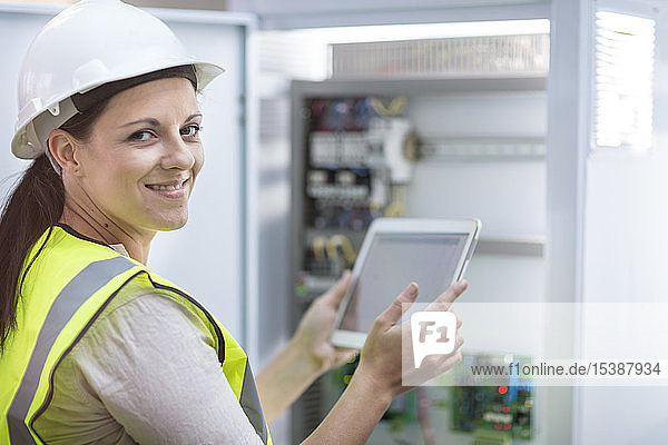 Porträt einer lächelnden Technikerin mit Tablette bei der Arbeit an einer Kiste mit Leiterplatten