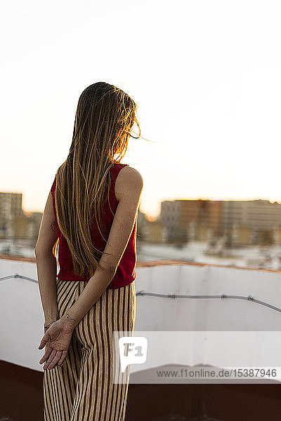Rückansicht eines jugendlichen Mädchens  das bei Sonnenuntergang auf einer Dachterrasse in der Stadt steht