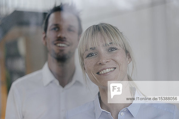 Successful businesswoman and businessman looking out of window  smiling