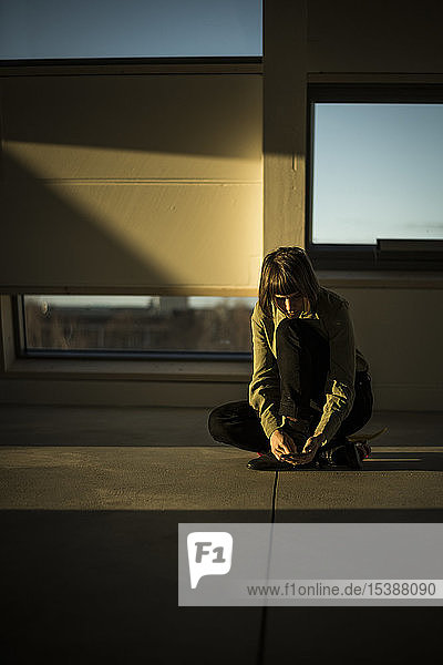 Businesswoman sitting on office floor at sunset using smartphone