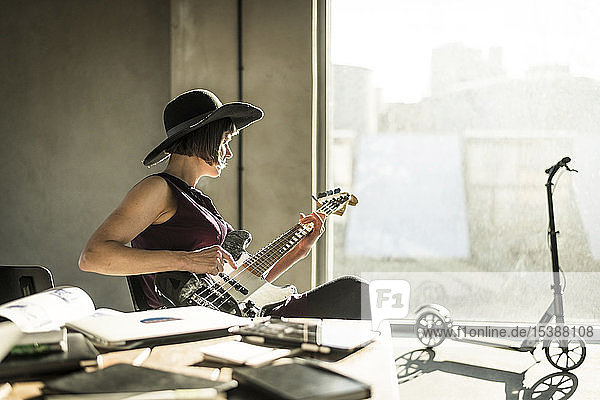 Woman with hat sitting in office  playing he guitar