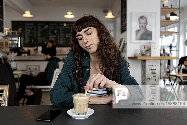 Junge Frau mit Milchkaffee  die in einem Café am Tisch sitzt
