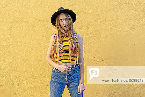 Porträt eines verärgerten Teenager-Mädchens mit Hut an gelber Wand