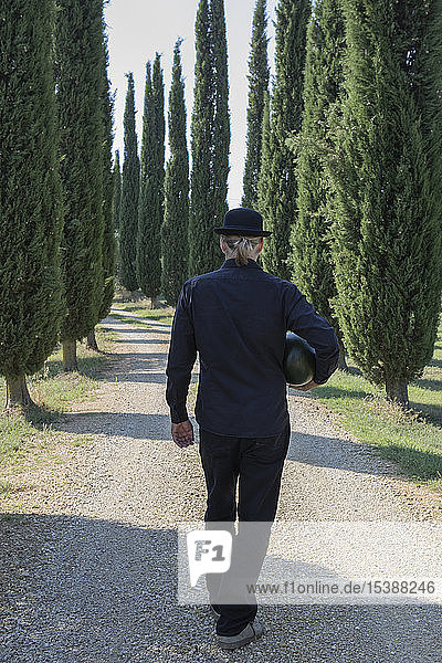 Italy  Tuscany  rear view of man surrounded by cypresses wearing a bowler hat holding a melon