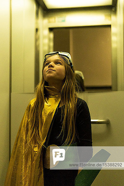 Mädchen im Kostüm einer Superheldin im Aufzug  nach oben schauend