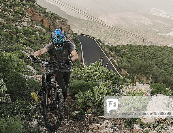 Spain  Lanzarote  mountainbiker pushing his bike on a trail in the mountains