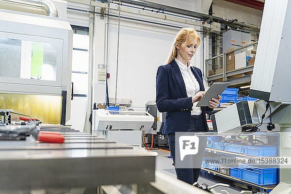 Businesswoman using tablet at machine in factory