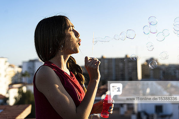 Teenager-Mädchen bläst bei Sonnenuntergang Seifenblasen auf einer Dachterrasse in der Stadt