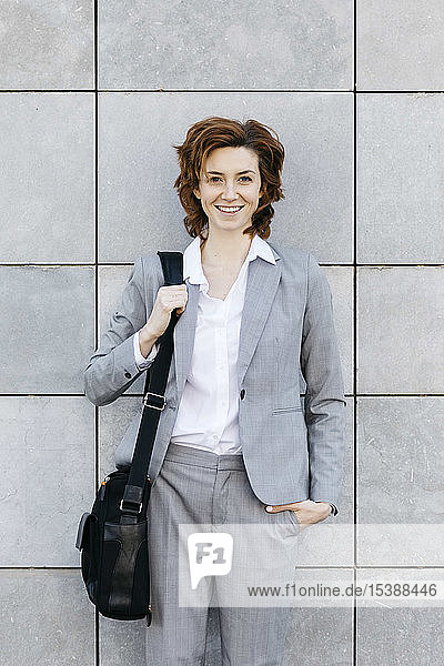 Porträt einer jungen selbstbewussten Geschäftsfrau vor grau gekachelter Wand