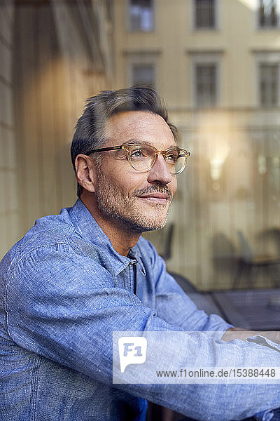 Porträt eines Brillenträgers hinter einer Fensterscheibe
