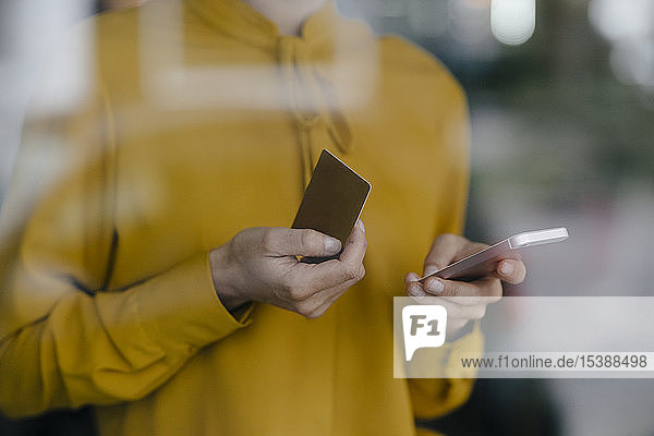 Blonde Geschäftsfrau sitzt am Fenster und bezahlt mit Smartphone und Kreditkarte