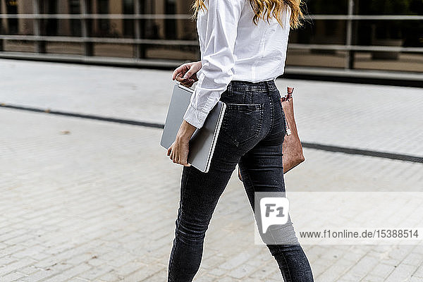 Junge Geschäftsfrau  die mit einem Laptop durch die Stadt läuft