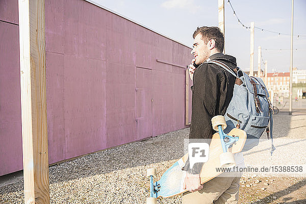 Junger Mann mit Skatebaord und Handy in der Stadt unterwegs