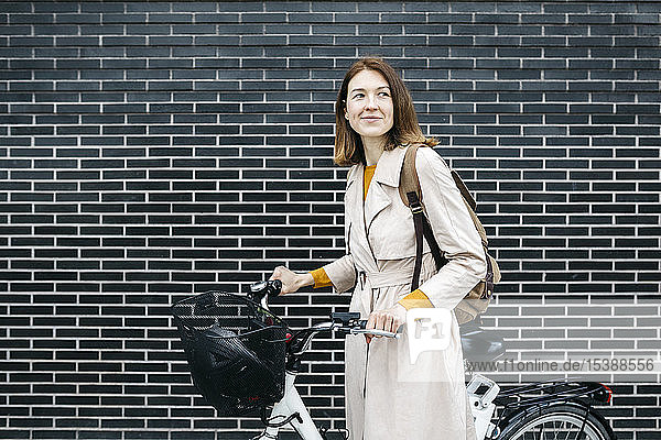 Lächelnde Frau mit E-Bike an einer Ziegelmauer