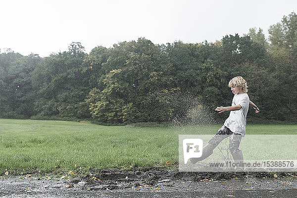 Junge spritzt mit schmutzigem Pfützenwasser