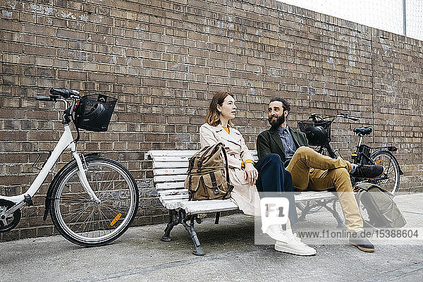 Ehepaar sitzt auf einer Bank neben E-Bikes und unterhält sich