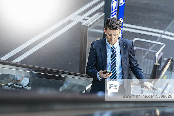 Businessman with suitcase and cell phone on escalator