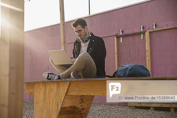 Young man sitting on platform using laptop