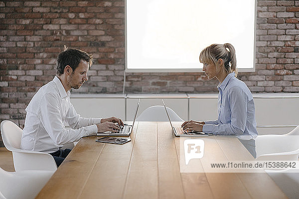 Geschäftsmann und -frau sitzen am Schreibtisch und arbeiten am Laptop