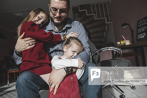 Father cuddling with two daughters at home
