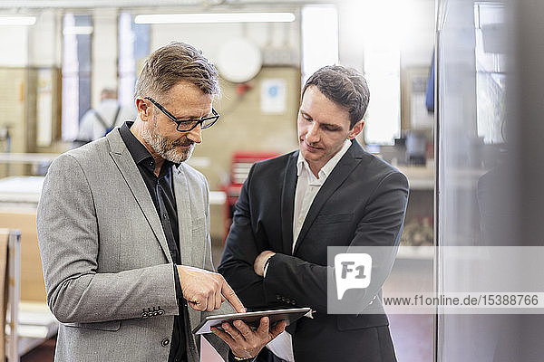Zwei Geschäftsleute mit Tablette diskutieren in einer Fabrik