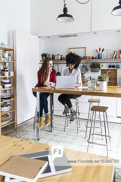 Zwei Frauen arbeiten gemeinsam in der Küche  benutzen einen Laptop und diskutieren über Dokumente