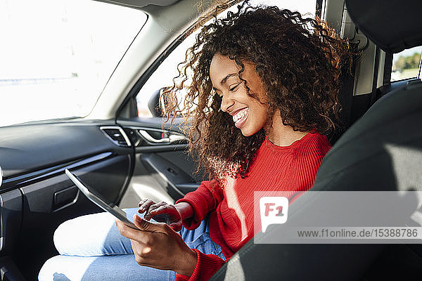 Glückliche junge Frau mit Tablette im Auto
