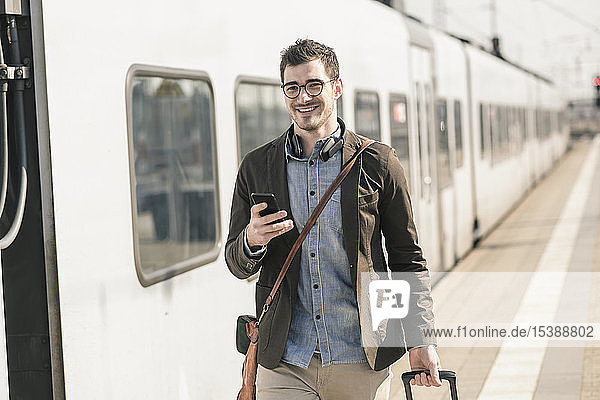 Lächelnder junger Mann mit Handy am Bahnsteig