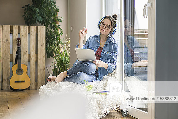 Woman with headphones and laptop sitting at the window at home