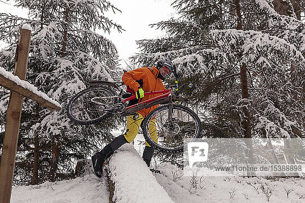 Mann mit Mountainbike überquert umgefallenen Baum auf Weg im Winterwald