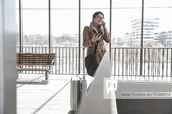 Businesswoman with baggage and cell phone applying earphones