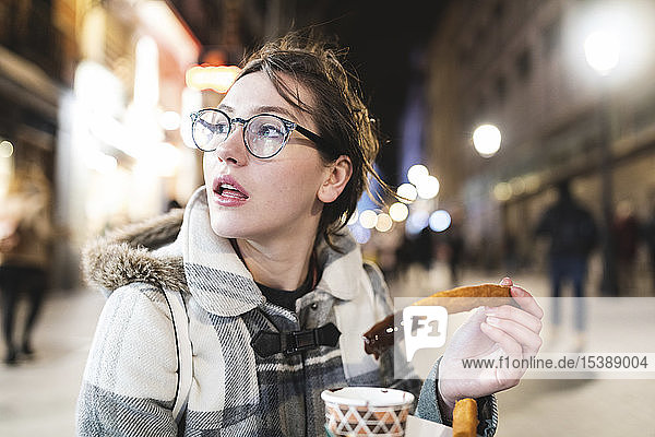 Spain  Madrid  young woman in the city at night eating typical churros with chocolate