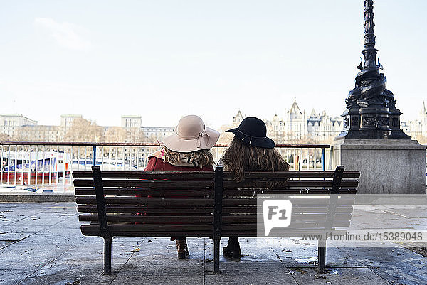 UK London rear view of two women sitting on a bench at River Thames promenade