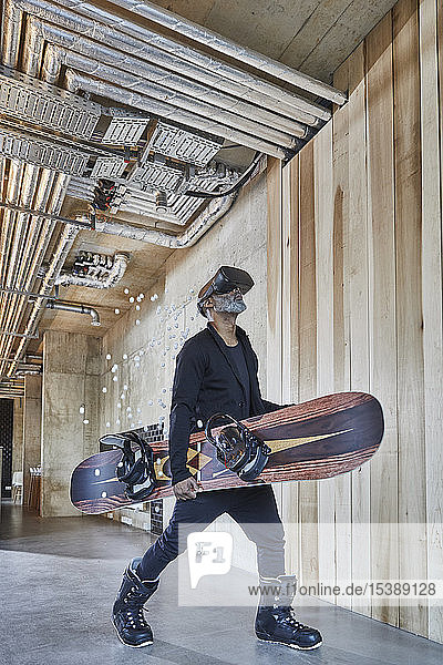 Mature businessman wearing VR glasses holding snowboard in modern office