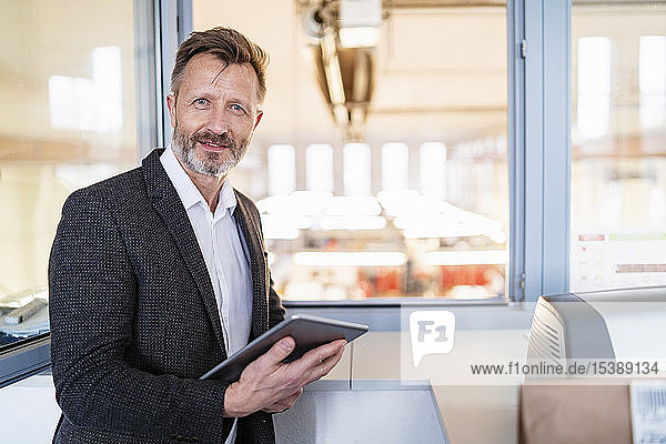 Porträt eines Geschäftsmannes mit Tablett am Fenster mit Fabrikhintergrund