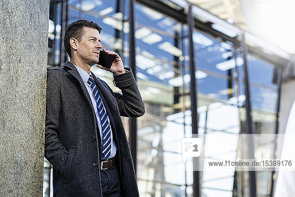 Businessman on cell phone leaning against a wall