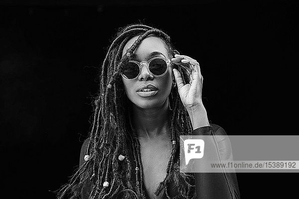 Bildnis einer Frau mit Dreadlocks mit Sonnenbrille vor schwarzem Hintergrund