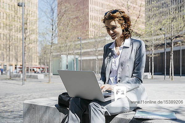 Junge Geschäftsfrau mit roten Schuhen  die auf einer Bank in der Stadt sitzt und am Laptop arbeitet