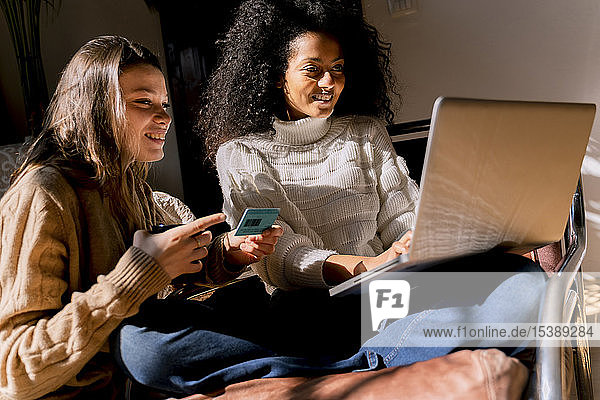 Freunde sitzen auf der Couch  benutzen einen Laptop und bezahlen mit Kreditkarte
