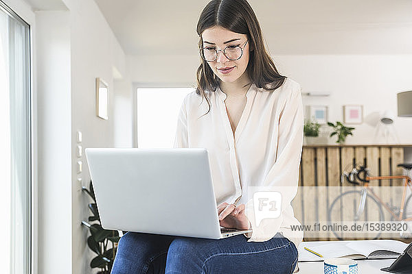 Junge Frau sitzt zu Hause mit Laptop am Tisch