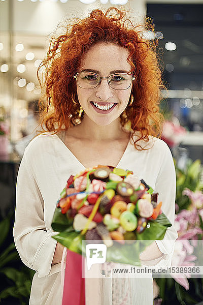 Porträt einer lächelnden Frau  die in einem Geschäft einen Bonbonstrauss hält